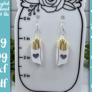 May include: A pair of silver dangle earrings with a white and brown french fry design and a gray heart on each earring. The earrings are displayed on a white background with a ruler measuring in inches.