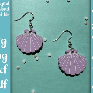 Op de afbeelding: Een paar paarse schelp-oorbellen met zilveren haakjes. De oorbellen zijn op een lichtblauwe achtergrond met witte glitter.