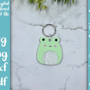 May include: A light green frog keyring with a white circle in the middle. The keyring is attached to a silver ring.
