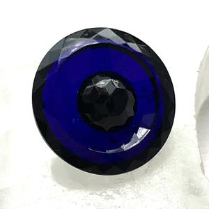 May include: A faceted, round glass knob with a deep blue center and a black, textured center. The outer edge is black and faceted, creating a sparkling effect. This decorative knob is suitable for furniture or cabinet doors.
