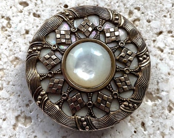 Pearl button with ornate brass overlay.