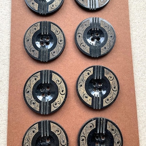 May include: A set of eight round black buttons arranged in two columns. Each button features a central four-hole design, vertical raised ridges at the top and bottom, and gold-colored engraved scrollwork patterns on the sides.