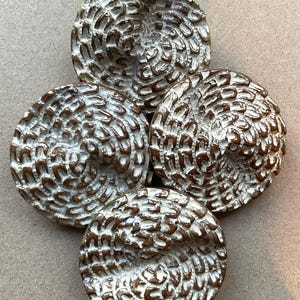 May include: Four circular buttons arranged in a cluster, each featuring a raised, swirling pattern of dark brown grooves contrasted against a textured white surface. The design creates a repetitive, scale-like appearance across the round faces.