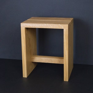 Peut inclure: Un tabouret en bois de couleur claire avec un design simple et moderne. Le tabouret a un cadre carré avec une poutre de support horizontale. Le dessus est fait de trois planches de bois parallèles. Le tabouret est en bois clair.