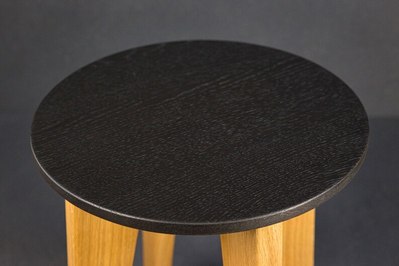 K&ouml;nnte beinhalten: Kleiner, runder Beistelltisch mit einer schwarzen, strukturierten Tischplatte und drei hellen Holzbeinen. Das Design des Tisches ist schlicht und modern, passend f&uuml;r verschiedene Einrichtungsstile. Die Tischplatte hat einen Durchmesser von ca. 38 cm.