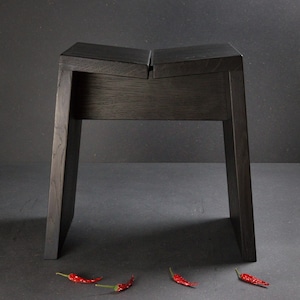 Peut inclure: Un tabouret en bois teinté foncé avec un siège divisé. Le tabouret a un cadre rectangulaire avec des pieds inclinés. Trois piments rouges sont éparpillés sur le sol devant le tabouret.