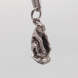 Peut inclure: Breloque en argent représentant un singe assis sur une base. Le singe est détaillé et a une apparence réaliste.