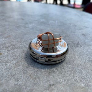 Puede incluir: Un porta anillos de plata con un anillo de piedra blanca envuelto en alambre de cobre.