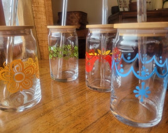 Puede incluir: Cuatro tarros de vidrio para beber con tapas de madera y pajitas. Cada tarro tiene un diseño floral colorido diferente. Los diseños son naranja, verde, rojo y azul.