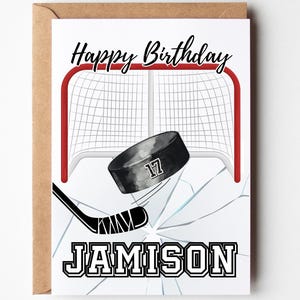 May include: Happy Birthday card with a hockey theme. The card features a hockey puck with the number 17 on it, a hockey stick, and a hockey net. The card is white with a brown envelope. The name Jamison is written on the card.