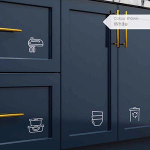 Può includere: Ante di cucina blu scuro con ferramenta dorata. Icone bianche di un mixer, un contenitore per alimenti, ciotole e un cestino per il riciclaggio sono sulle ante. Il testo "Colour shown: White" è in una freccia bianca.