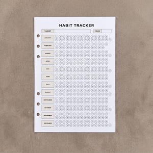 May include: A white paper habit tracker insert with six binder holes on the left side. The header reads HABIT TRACKER with fields for TARGET and YEAR. Twelve rows labelled January through December contain numbered circles from 1 to 31 for daily tracking.