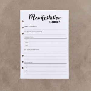 May include: A white paper planner insert with six punched holes along the left edge. The header reads Manifestation Planner. Sections include I WANT TO MANIFEST, MY PRAYER TO THE UNIVERSE, VISUALIZATION, MY DAILY AFFIRMATIONS, and ACTION PLAN.