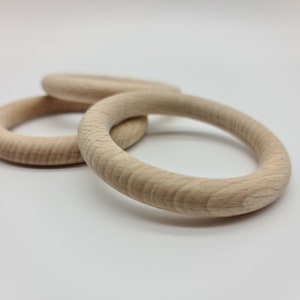 Könnte beinhalten: Drei Holzringe, wahrscheinlich für ein Baby oder Kleinkind, liegen auf einer weißen Oberfläche. Die Ringe sind aus hellem Holz gefertigt, mit sichtbarer Maserung und einer glatten, abgerundeten Form. Die Ringe liegen eng beieinander, was auf ein Spielzeug oder Bastelprojekt hindeutet.