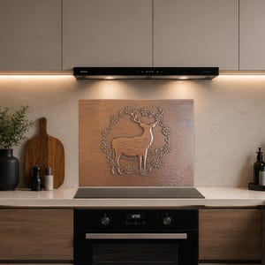 May include: A rectangular copper-toned kitchen backsplash panel featuring a central embossed design of a standing deer encircled by a floral wreath. The panel is positioned behind a black induction cooktop in a modern kitchen setting.