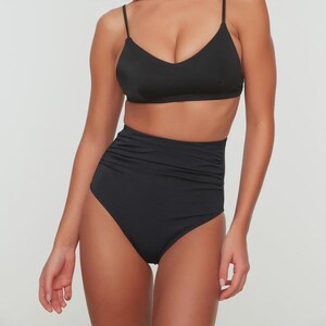 May include: Black two-piece swimsuit. The top has a V-neckline and thin straps. The high-waisted bottoms feature a ruched design. The swimsuit is made of a smooth, solid black fabric.
