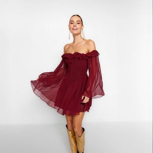 May include: A burgundy off-the-shoulder dress with ruffled detailing and long, flowing sleeves. The dress has a fitted bodice and a flowing skirt.