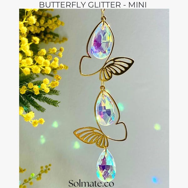 May include: A gold-colored butterfly-shaped ornament with three iridescent crystal teardrops. The ornament is suspended, and the text "BUTTERFLY GLITTER - MINI" is at the top. The website "Solmate.co" is at the bottom.