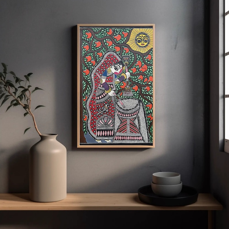 Pu&ograve; includere: Un dipinto Madhubani colorato che raffigura una donna in un sari rosso e rosa, che tiene un bastone e sta in piedi davanti a un grande oggetto grigio con motivi. Il dipinto &egrave; su uno sfondo di foglie verdi e un sole giallo con un viso.