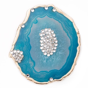 May include: A teal blue agate slice with gold trim and clear rhinestones. The agate has a natural pattern of white and gray swirls.