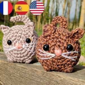 Peut inclure: Deux peluches de chat en crochet, l'une brune et l'autre brun clair, avec du fil blanc pour les moustaches et un nez rose. Les peluches ont des yeux en boutons noirs.