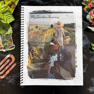 Könnte beinhalten: Ein spiralgebundenes Notizbuch mit dem Titel My Garden Journey und einem Titelbild einer Person mit Sonnenhut, die mit Körben durch ein Feld geht. Das Notizbuch ist umgeben von Gartengeräten, Samentüten, einer floralen Büroklammer und einem Stift.