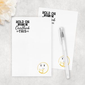 May include: Two white notepads with the text "HOLD ON LET ME OVERTHINK THIS" in black. A yellow thinking emoji is at the bottom. A clear pen rests on one notepad.