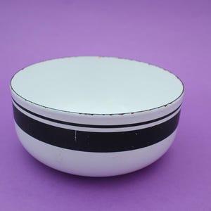 Puede incluir: Cuenco de esmalte blanco con diseño de rayas negras. El cuenco tiene forma redondeada y borde negro. El interior es blanco y el exterior presenta una ancha banda negra. Un artículo de cocina vintage.