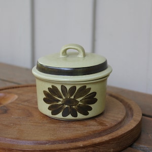 Pode incluir: Um pequeno a&ccedil;ucareiro redondo de cer&acirc;mica com tampa. O a&ccedil;ucareiro &eacute; decorado com um desenho floral castanho e verde. A tampa tem uma faixa castanha em volta da parte superior.