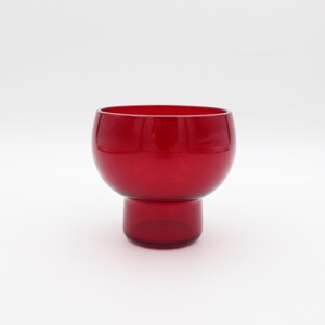 May include: A vibrant red glass bowl with a rounded top and a smaller, cylindrical base. The bowl has a smooth, glossy finish and is set against a plain white background. This decorative piece could be used for serving or display.