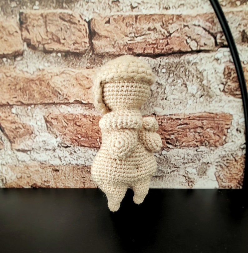 May include: A crocheted doll with a cream-colored body and a white crocheted hat. The doll is standing on a black surface.