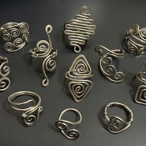 May include: A collection of ten silver wire rings with different designs, including spirals, geometric shapes, and abstract forms.