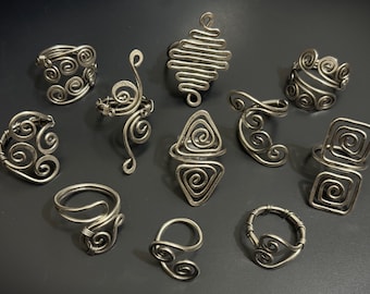 May include: A collection of ten silver wire rings with different designs, including spirals, geometric shapes, and abstract forms.