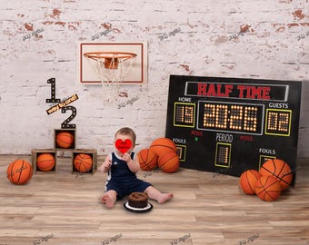 Könnte beinhalten: Ein Basketball-Foto-Setup mit einem Miniaturkorb, einer Anzeigetafel und Basketbällen. Ein Baby in einem marineblauen Outfit sitzt in der Nähe eines kleinen Kuchens. Die Anzeigetafel zeigt "HALF TIME" und die Ergebnisse.