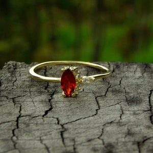 May include: A gold ring with a red oval-shaped gemstone and smaller clear gemstones on the band.