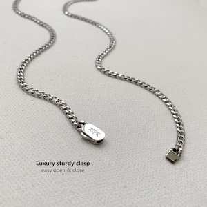 May include: A silver-colored chain necklace with a sturdy clasp. The clasp is rectangular with the letters "AYK" engraved on it. The text "Luxury sturdy clasp easy open & close" is visible below the necklace.