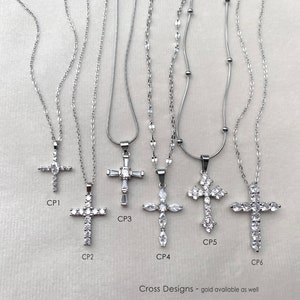 May include: Six silver-toned necklaces with cross pendants labeled CP1 through CP6. Each pendant features clear, faceted stones in various arrangements, including marquise and baguette cuts, suspended on delicate silver-toned metal chains.