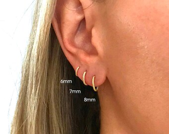 May include: Close-up of a person's ear with three gold hoop earrings in different sizes: 6mm, 7mm, and 8mm. The earrings are all made of a thin, twisted wire.