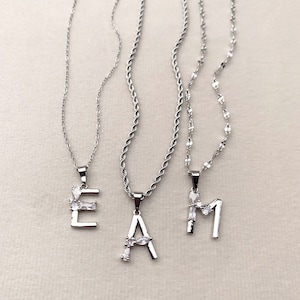 May include: Three silver necklaces with letter pendants. The pendants are adorned with small clear cubic zirconia stones. The letters are E, A, and M.