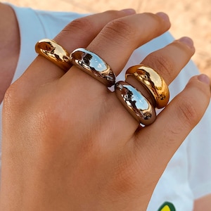 May include: Four gold and silver rings stacked on a finger. The rings are all smooth and rounded, with a slightly domed shape.
