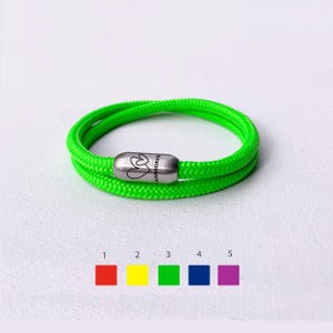 May include: A neon green rope bracelet with a silver magnetic clasp. The clasp is engraved with two hearts and the text "ANN&DAVE". The bracelet is shown on a white background with color swatches below.