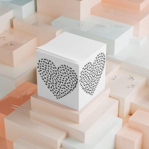 May include: A white cube notepad featuring a black heart design made of cat silhouettes. The notepad sits on a pastel-coloured geometric structure, with silver paper clips scattered around. The design is modern.