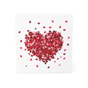 May include: A white square box with a red heart made of smaller red, pink, and white hearts. The heart is in the center of the box.