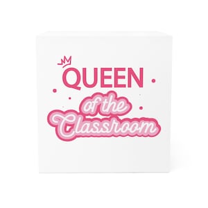 May include: A white cube with the words "QUEEN of the Classroom" in pink and light pink lettering. A small pink crown is above the word "QUEEN". Dots and swirls are scattered around the text.