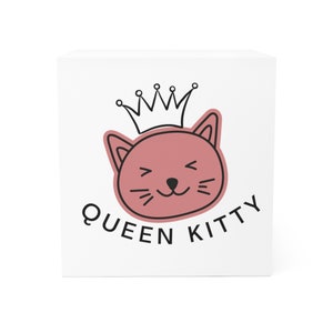 May include: A white square box with a pink cat wearing a black crown and the text "QUEEN KITTY".