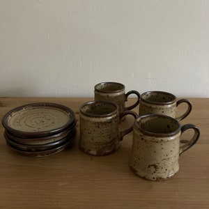 May include: Set of four brown and beige speckled ceramic coffee mugs with four matching saucers. The mugs have brown handles.