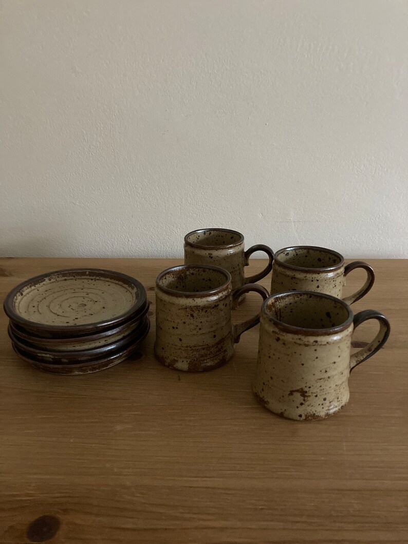 May include: Set of four brown and beige speckled ceramic coffee mugs with four matching saucers. The mugs have brown handles.