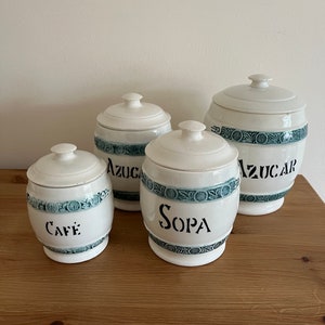 May include: Set of four white ceramic canisters with blue and green floral designs. The canisters are labelled "Cafe", "Sopa", "Azucar", and "Azucar".