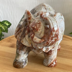 May include: A hand-carved stone elephant figurine with a white, brown, and red marbled pattern. The elephant is standing with its trunk raised and its eyes closed.