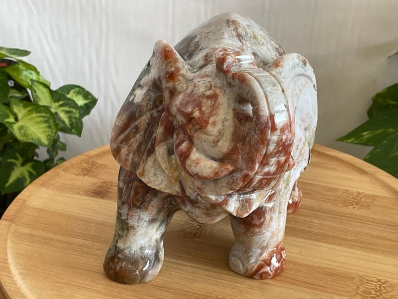 May include: A hand-carved stone elephant figurine with a white, brown, and red marbled pattern. The elephant is standing with its trunk raised and its eyes closed.